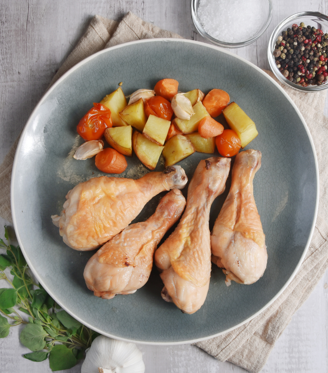 4 deliciously cooked Fox River Australian Free-Range Chicken Drumsticks with tomato, carrot and garlic on a blue plate