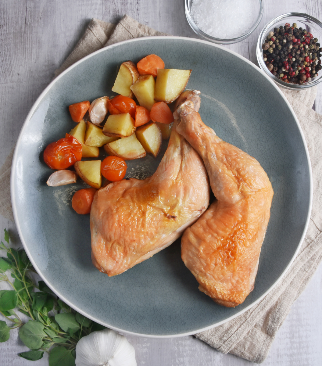 Deliciously cooked Australian Free-Range Whole Chicken Legs with tomato, carrot and potato on a blue plate