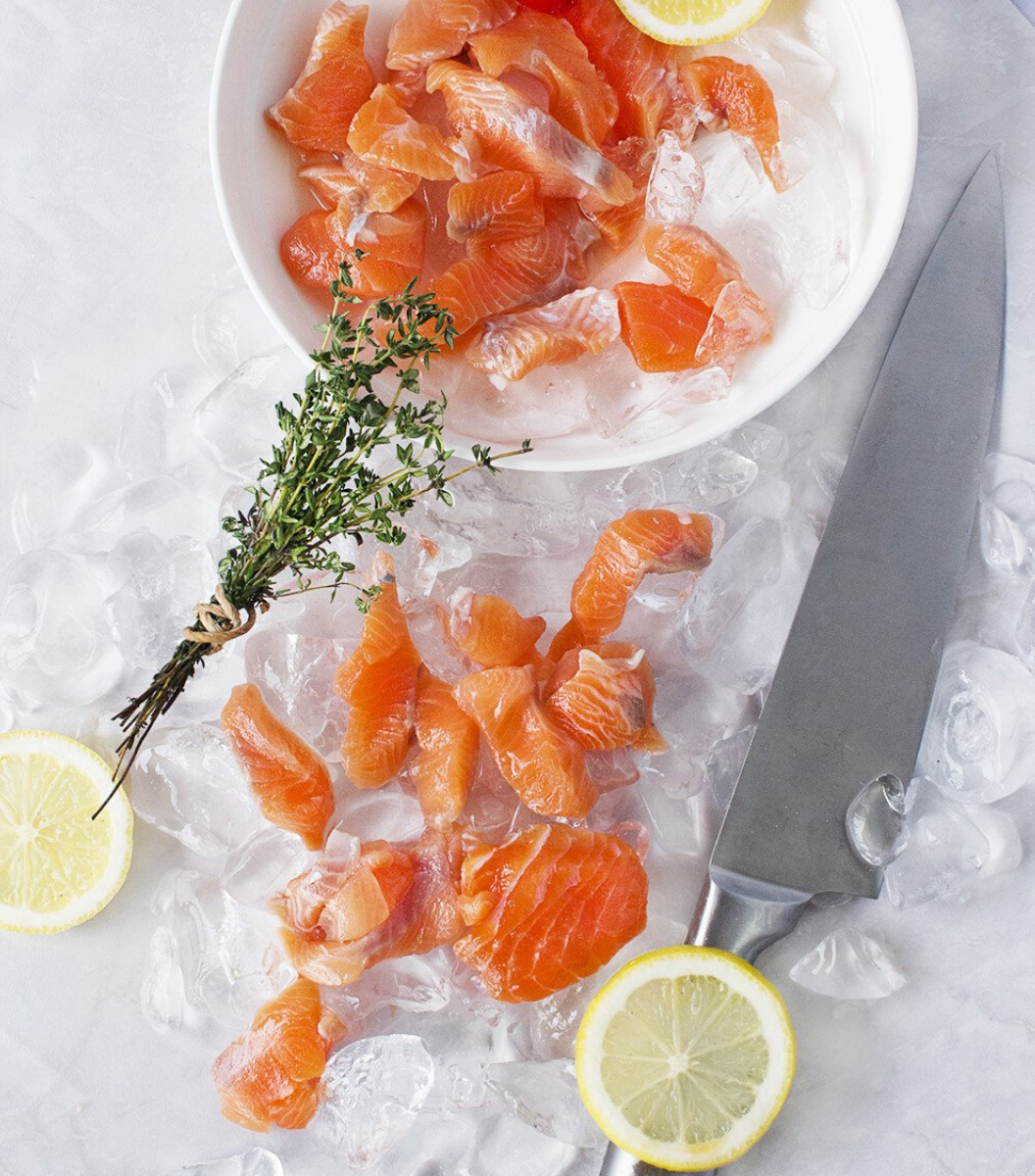 Fresh Mt. Cook Alpine New Zealand Salmon Pieces with ice cube, lemon slices and a japanese white steel knife by aside