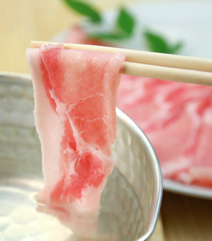 
                  
                    A pair of chopsticks holding a slice of fresh pork shabu shabu
                  
                