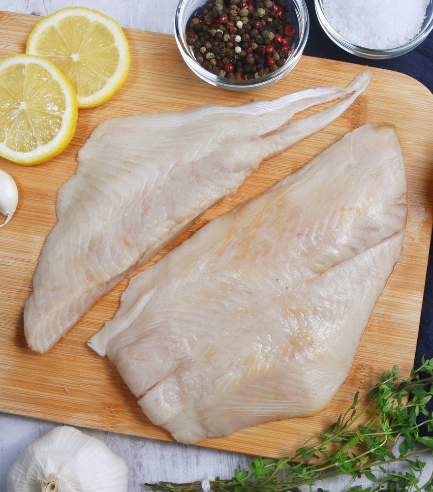 2 fresh New Zealand Ray Bream Fillet on a wooden board with lemon sliced, garlic and spices aside